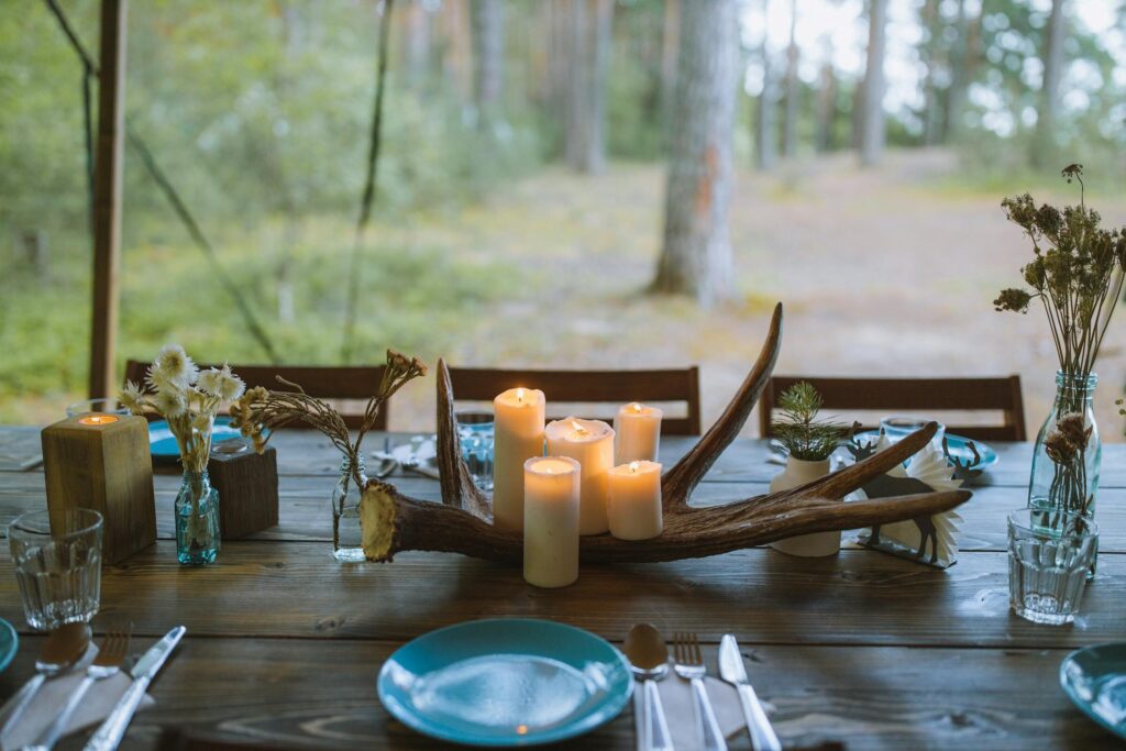 A rustic dining table set outdoors with candles, floral arrangements, and wooden decor.